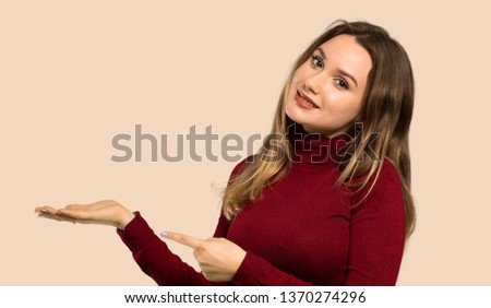 Teenager girl with turtleneck holding copyspace imaginary on the palm to insert an ad over isolated ocher background