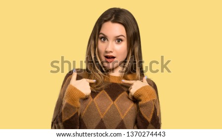 Teenager girl with brown sweater with surprise facial expression over isolated yellow background