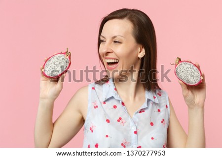 Cheerful young woman looking aside, holding halfs of fresh ripe pitahaya, dragon fruit isolated on pink pastel background in studio. People vivid lifestyle relax vacation concept. Mock up copy space
