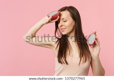 Beautiful young woman keeping eyes closed holding fresh ripe pitahaya dragon fruit isolated on pink pastel wall background in studio. People vivid lifestyle relax vacation concept. Mock up copy space