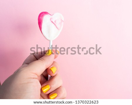 A woman with yellow painted nails with a lollipop in her hand and pastel pink background
