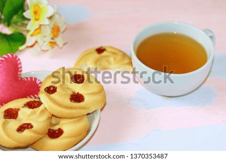 Shortbread with cherry jam and pink heart on a saucer, a mug of tea on a pink-blue table.