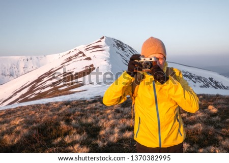 Photographer in yellow jacket taking photo on snowy winter field