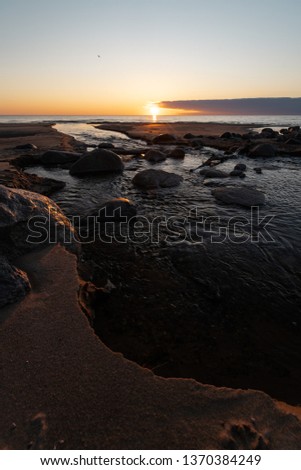 Beautiful sunset with red sand and spring water from a river exiting to the sea - Veczemju Klintis, Latvia - April 13, 2019