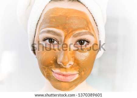 Cosmetics brown mask of clay on the beautiful young female face, isolated on white