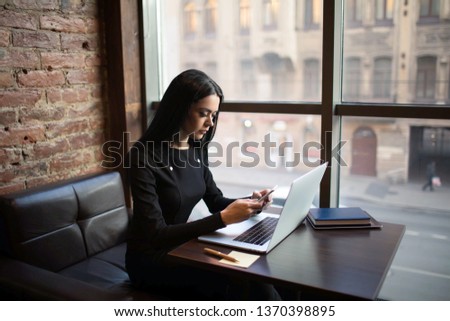 Woman government worker using apps on cellphone during training course on pc laptop computer, sitting in modern interior near big window with copy space. Female online payment via smartphone 