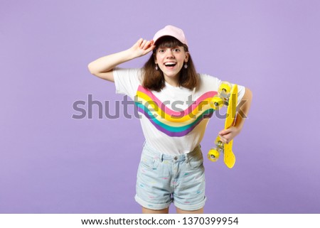 Portrait of funny teen girl in vivid clothes looking camera, holding yellow skateboard isolated on violet pastel background in studio. People sincere emotions, lifestyle concept. Mock up copy space