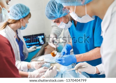 Group of surgeons at work operating in surgical theatre. Resuscitation medicine team wearing protective masks holding steel medical tools saving patient. Surgery and emergency concept