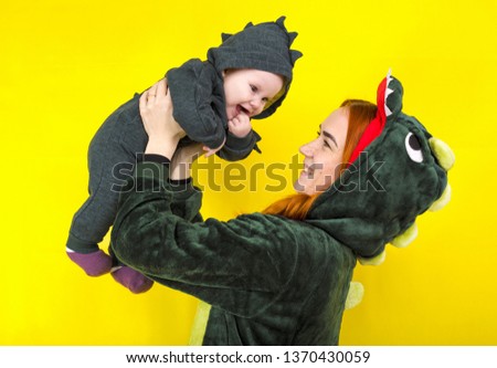 mom and daughter in a funny dragon costume. play on a yellow background. mother holds a little girl in a dragon costume over her head. happiness