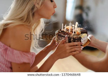 Beautiful happy Caucasian blonde woman blowing candles on birthday cake. Friends taking a gift to girl. Birthday party with friends concept