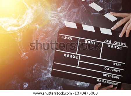 Close-up on an open clapperboard in hand before starting shooting a film with multi-colored smoke around with red and blue backlighting on a black isolated background
    
    - Image