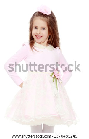 Dressy little girl long blonde hair, beautiful pink dress and a rose in her hair.She put hands on hips.Isolated on white background.