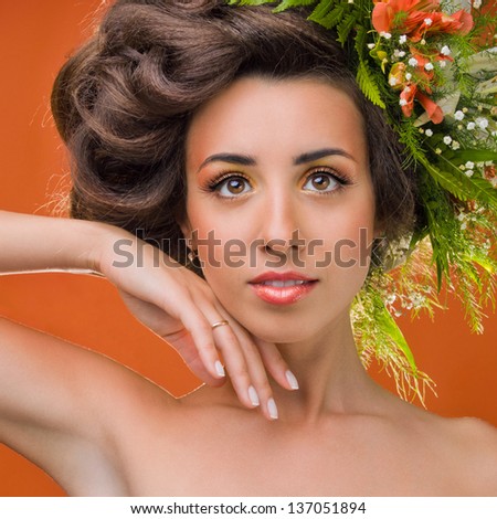 Studio portrait of a beautiful girl with flowers on her head on an orange background