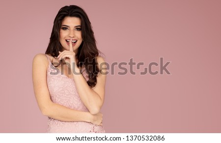 Attractive brunette lady posing in fashionable dress on a pink pastel studio backround.