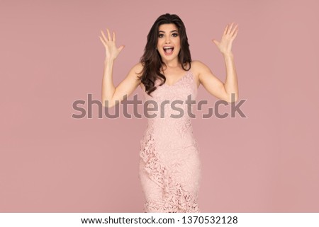 Attractive brunette lady posing in fashionable dress on a pink pastel studio backround.