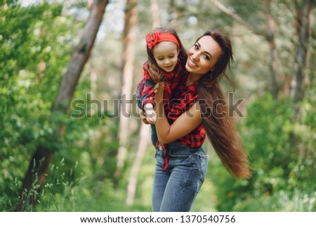 Young and very beautiful slim mum with long hair walking in a sunny summer park with her little beauties daughter