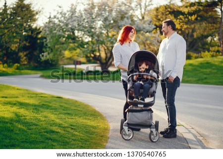 beautiful and stylish redhead mom in a white blouse wallking with her beautiful man dressed in a white shirt and blue jeans and they carry their little son in a cart