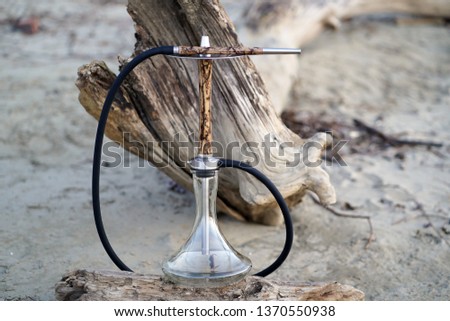                  Beige wooden hookah with lightning patterns from an electric current with a clean transparent bowl with a hose with metal elements on a log in the forest against the background of a f