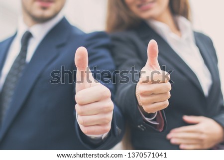 Successful young business people showing thumbs up sign, standing in front of his office.