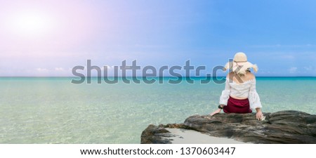 Tropical sea and unidentified woman sitting on the rock.