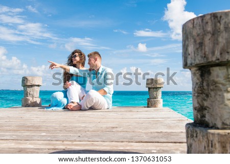 Couple having good time at the sea. They are sitting at the wooden pier, close to each other man pointing at something. Turquoise water is around them. Top angle picture. Vacations in Cancun.