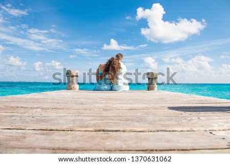 Couple siting at the wooden pier, hugging and looking at the turquoise water of caribbean sea in Cancun. Low angle picture.