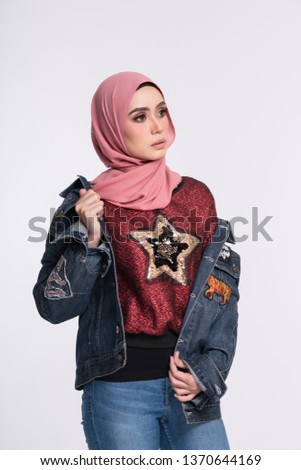 Fashionable young woman in jeans, long sleeves jeans jacket and hijab isolated on white background. Stylish Muslim female hijab fashion lifestyle portraiture concept.