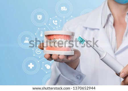A closeup of a dentist holding a denture model on her palm and a toothbrush in her hand at the medical service scheme background. The dentistry and odontology concept. Royalty-Free Stock Photo #1370652944