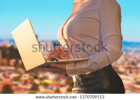 Woman in the office suit with a laptop on the balcony of the office building on the San Francisco city background.