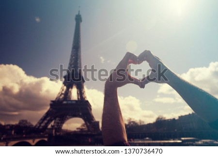 Love in Paris - hands forming a heart shape in front of the Eiffel Tower
