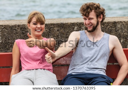 Young people friends in training suit with roller skates giving thumb up gesture. Woman and man relaxing on bench outdoor.