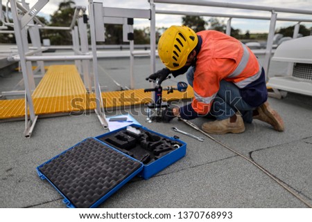 Approve certified testing engineer wearing  safety helmet protection conducting pull testing chemical abseiling anchor point prior used top of high rise building  construction site, Sydney, Australia