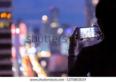 Woman using mobile phone taking cityscape photo at night
