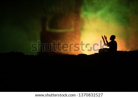 Silhouette of praying man with blurred mosque building on toned foggy background. Ramadan Kareem background. Muslim Eid holiday decoration. Praying people religion concept. Selective focus