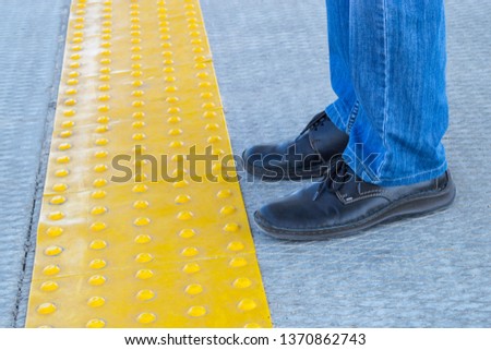 Man standing near the block tactile paving for blind handicap. Tactile marks for blind handicap on tiles pathway, walkway for blindness people. Man in jeans and boots.