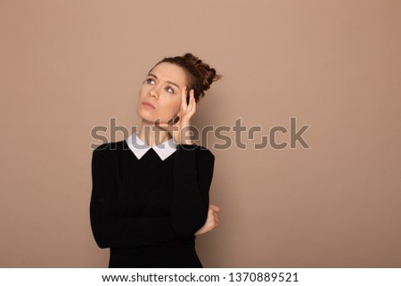 cute european girl with a bunch on her head is bored and looks away on a beige gray background