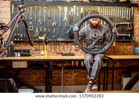 Portrait of a handsome repairman in workwear sitting with bicycle wheel at the workshop of a bike shop