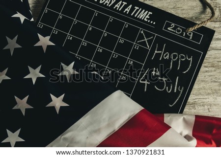 Overhead picture of calendar under united states flag, indicating the date 4th July 2019 in the calendar, all on wooden table, vintage style