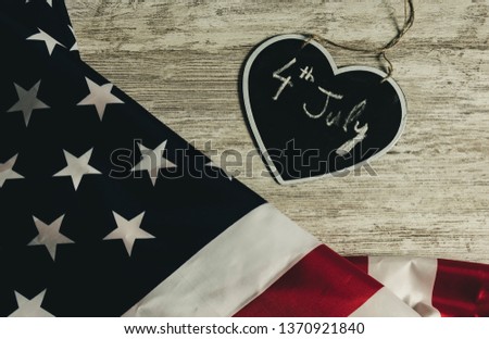 Overhead picture of united states flag and black heart including the date 4th July inside, all over wood table, vintage style
