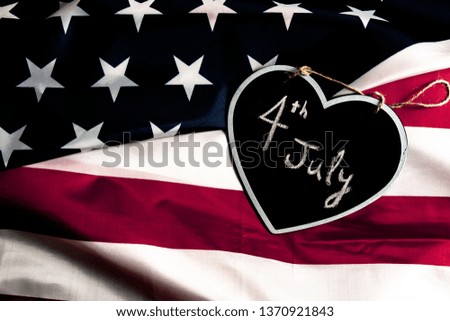 Overhead picture of black heart including the text of the date 4th July inside, on united states flag