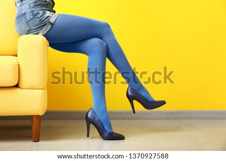 Stylish young woman in high heels sitting on armchair near color wall