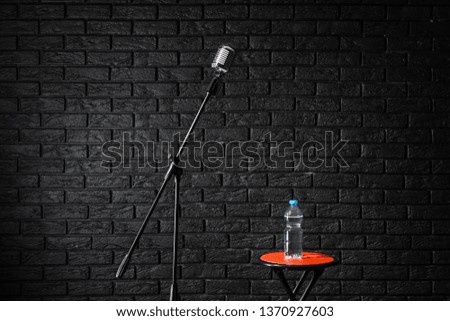 Microphone with stool and bottle of water on dark brick background