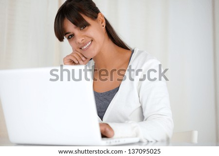 Portrait of a smiling young woman looking at you using her laptop computer