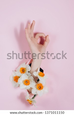 Hand show is showing a gesture Okay, ok, can be seen through a hole in pink paper with flowers. Body language concept.