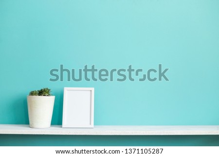 Modern room decoration with Picture frame mockup. White shelf against pastel turquoise wall with potted succulent plant.