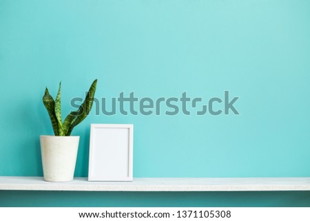 Modern room decoration with Picture frame mockup. White shelf against pastel turquoise wall with potted snake plant.