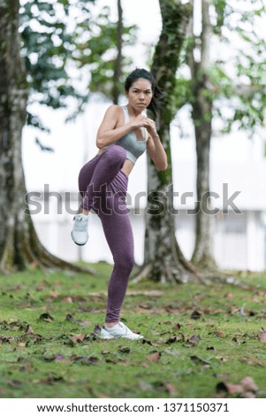 Young pretty slim fitness sporty woman doing kicking exercise during training workout outdoor at the park in the morning. Healthy lifestyle concept.
