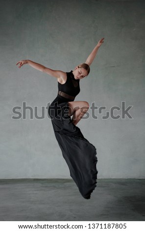 Young modern dancer in black dress. trains and dances in a gray studio Royalty-Free Stock Photo #1371187805