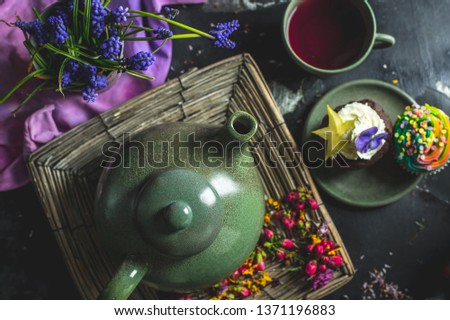 on a decorated with flower petals and flowers a dark wooden table, stands a kettle with tea, a cup and a chocolate cupcake