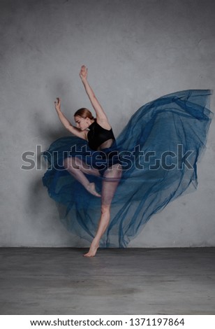 Young modern dancer in blue dress. trains and dances in a gray studio Royalty-Free Stock Photo #1371197864